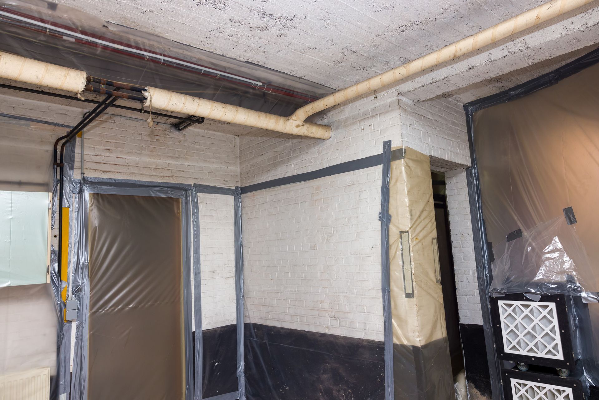 Basement interior with plastic sheeting, sealed doorway, pipes, and filter.