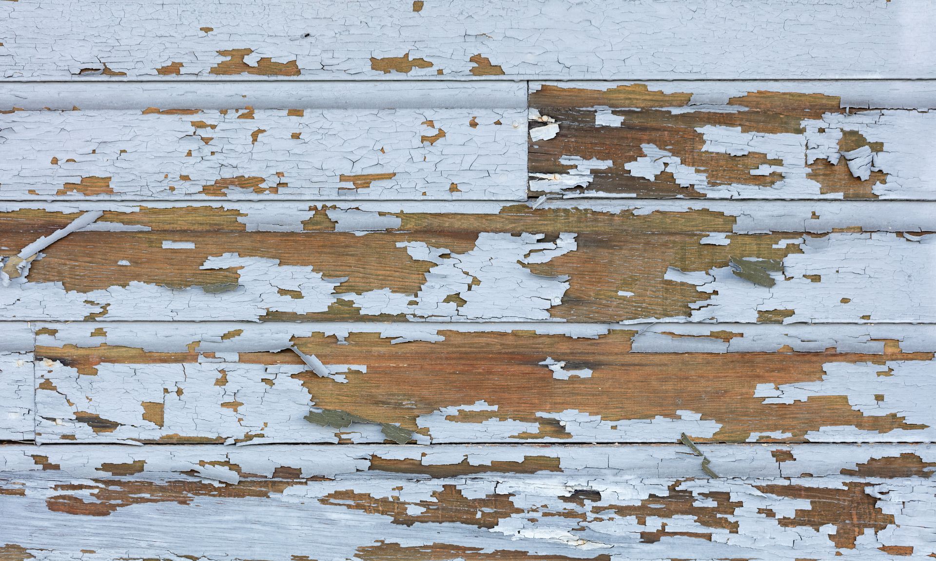 White, peeling paint on weathered horizontal wooden planks, exposing brown wood.