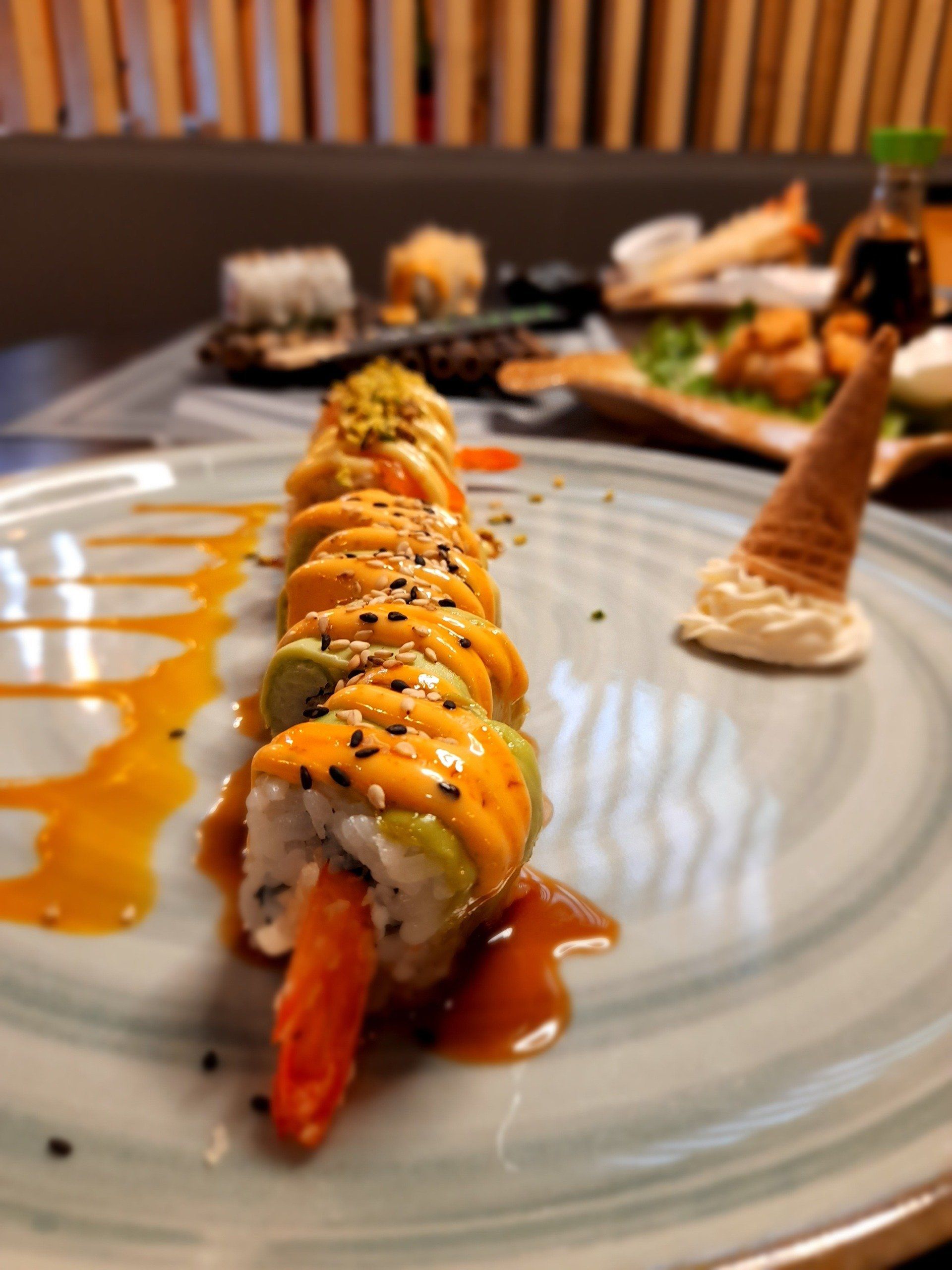 In un ristorante, un rotolo di sushi condito con salsa all'arancia su un piatto, con un dessert sullo sfondo.