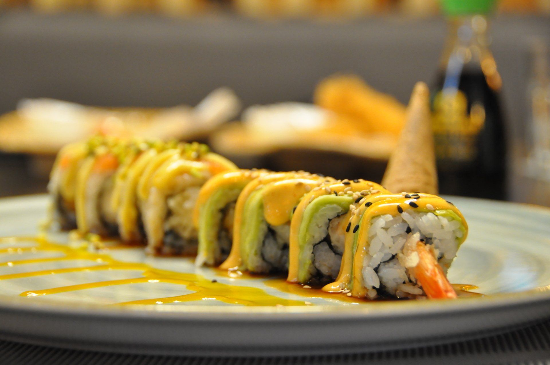 Sushi roll con salsa gialla su un piatto bianco in un ambiente da ristorante.