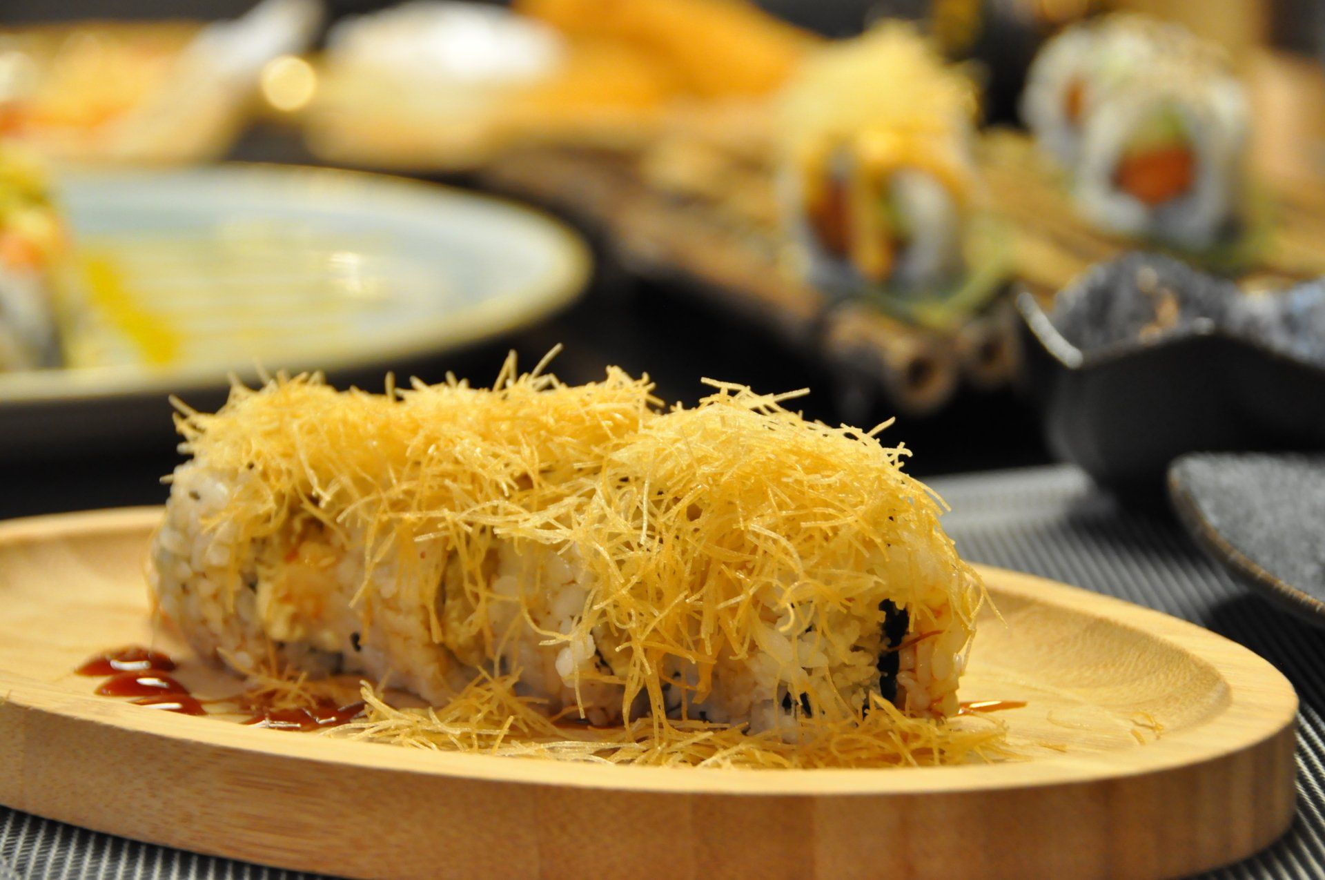 Sushi roll ricoperto di formaggio grattugiato su un piatto di legno in un ambiente da ristorante