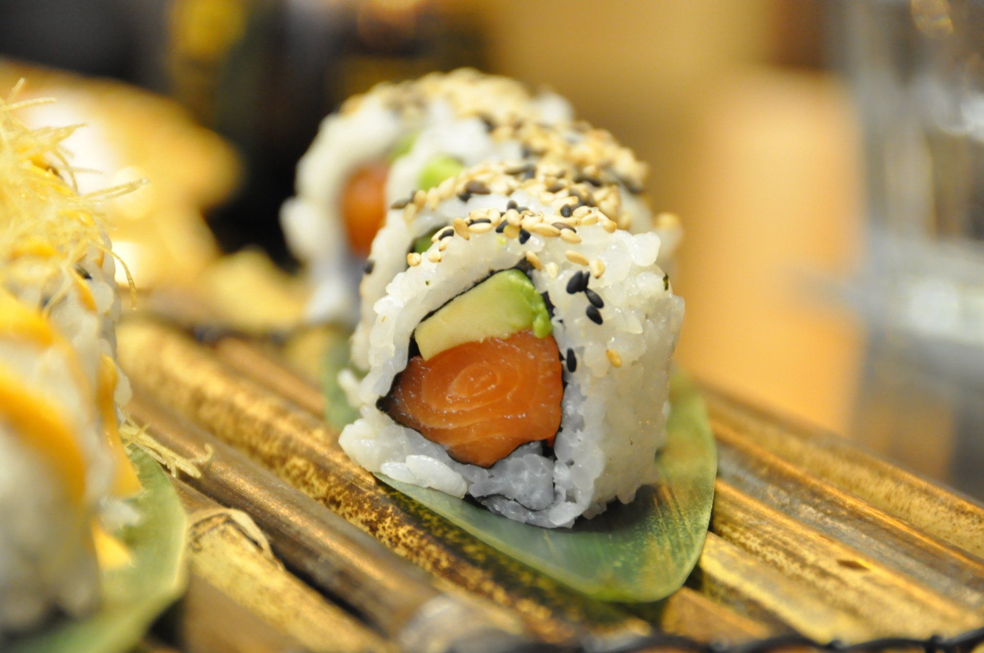 Primo piano di involtini di sushi con salmone all'arancia su un piatto decorativo di bambù.