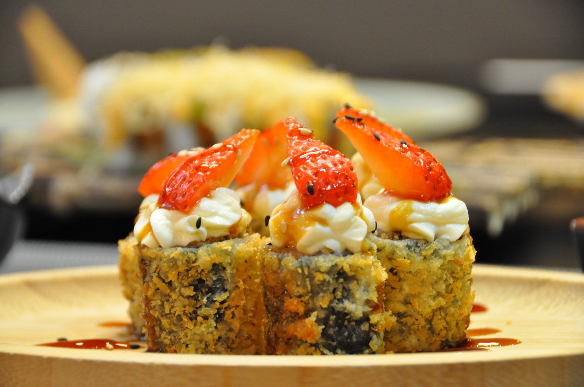 Rotoli di sushi con gamberi e salsa serviti su un piatto di legno.