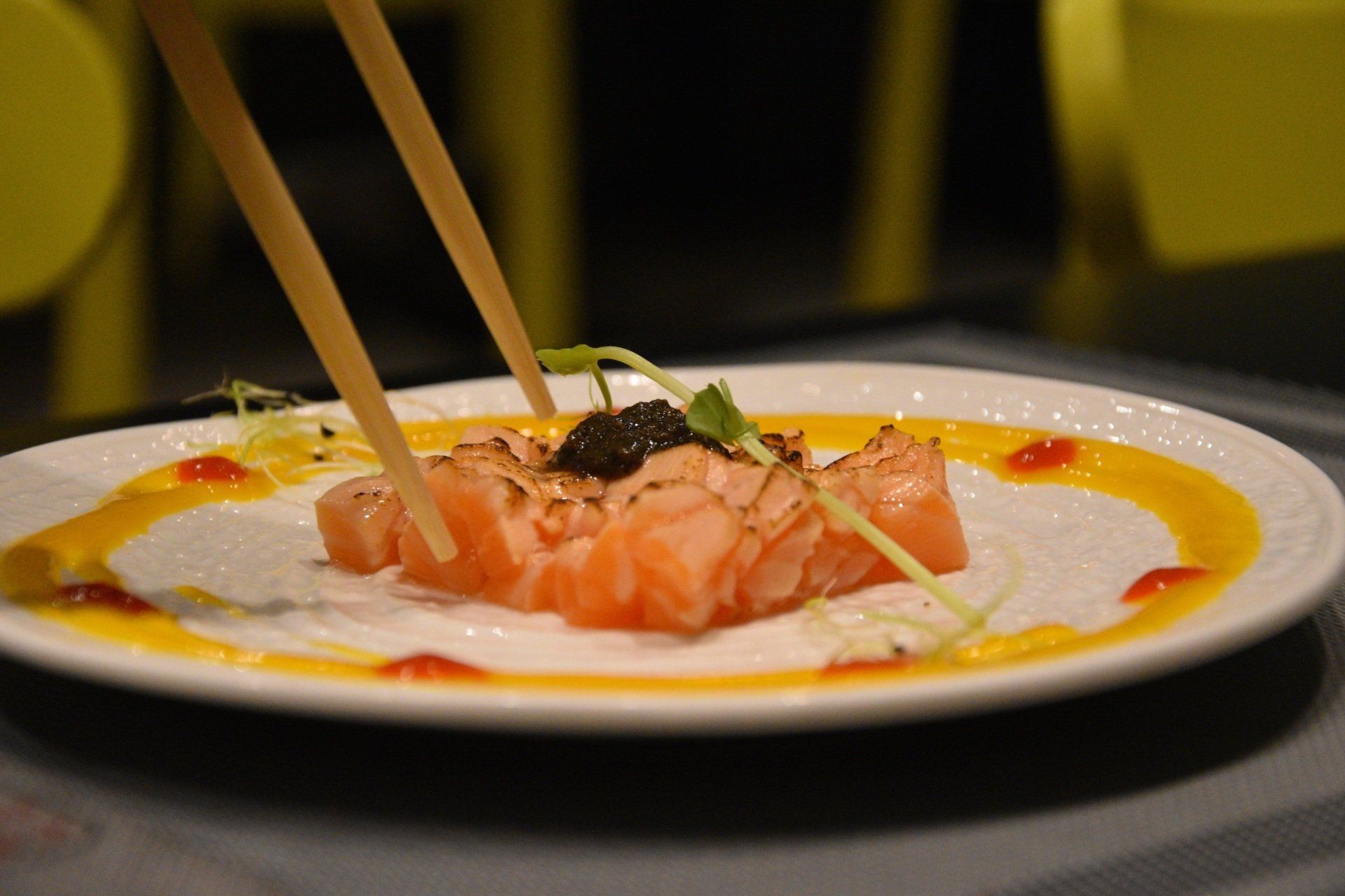 Sashimi di salmone servito con bacchette su un piatto bianco, condito con salsa.