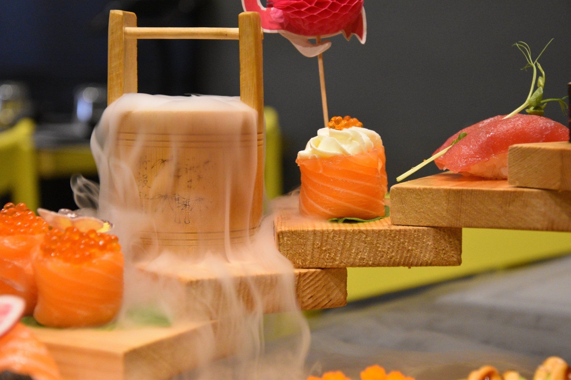 Pezzi di sushi su piattaforme di legno con una spruzzata di glassa bianca e uova di pesce arancioni brillanti, su una tavola sfocata.