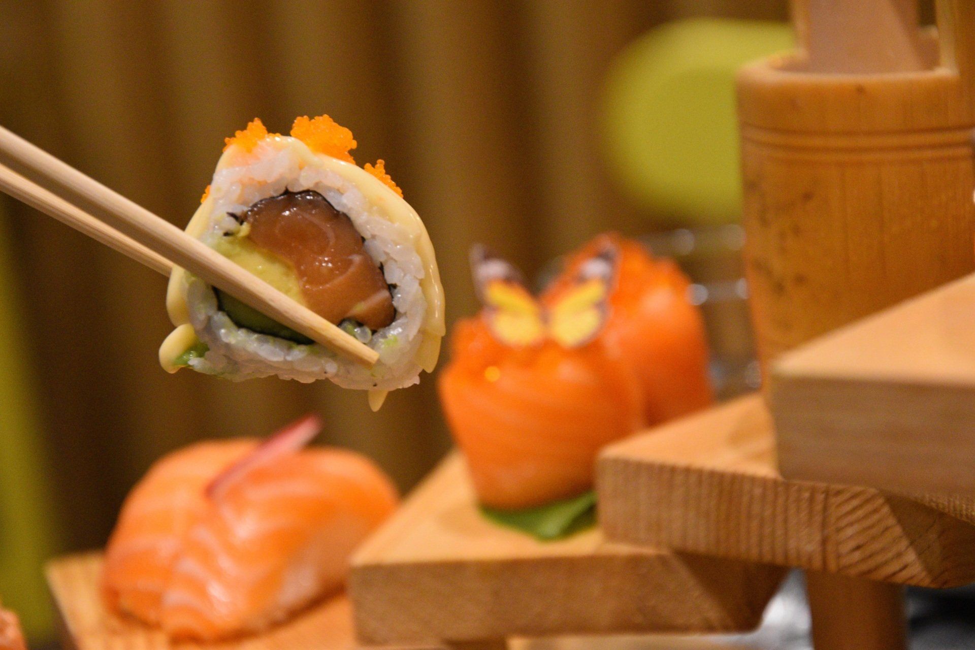 Sullo sfondo, bacchette che reggono un rotolo di sushi con nigiri di salmone su supporti di legno.