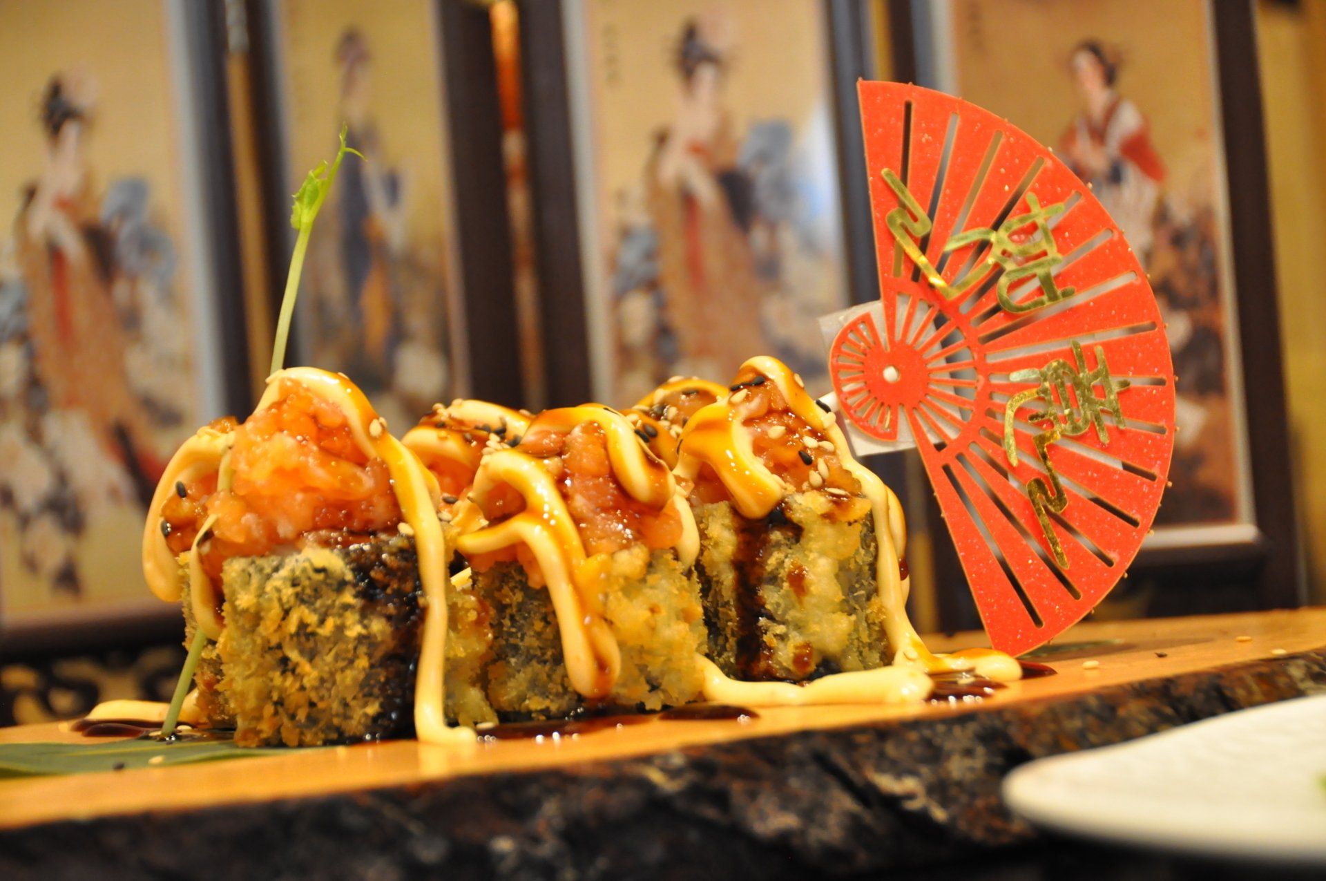 In un ristorante, dei rotoli di sushi conditi con salsa su un vassoio, decorati con un ventaglio di carta rossa.
