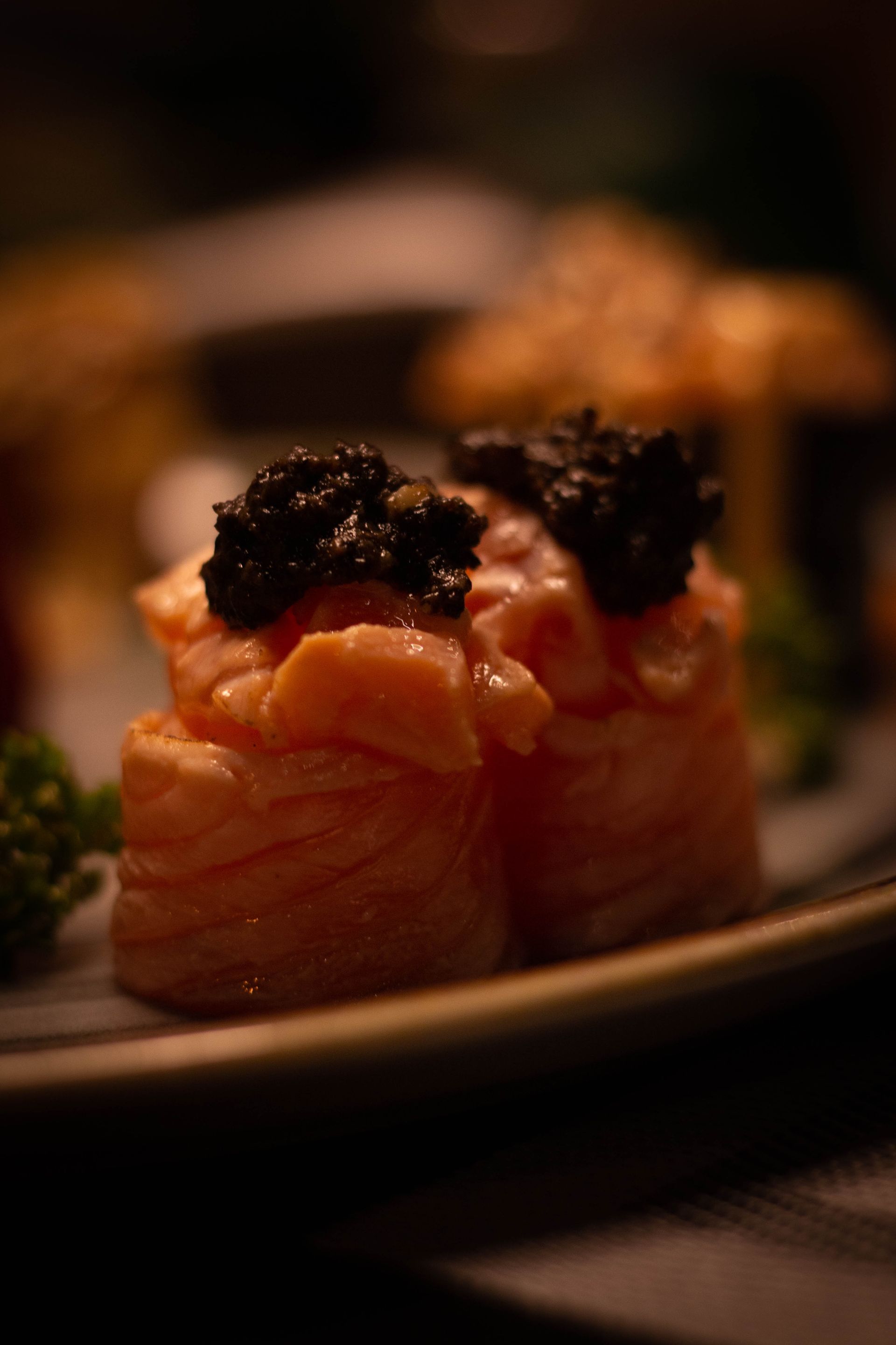 Due nigiri di sushi guarniti con una decorazione scura su un piatto scarsamente illuminato, primo piano