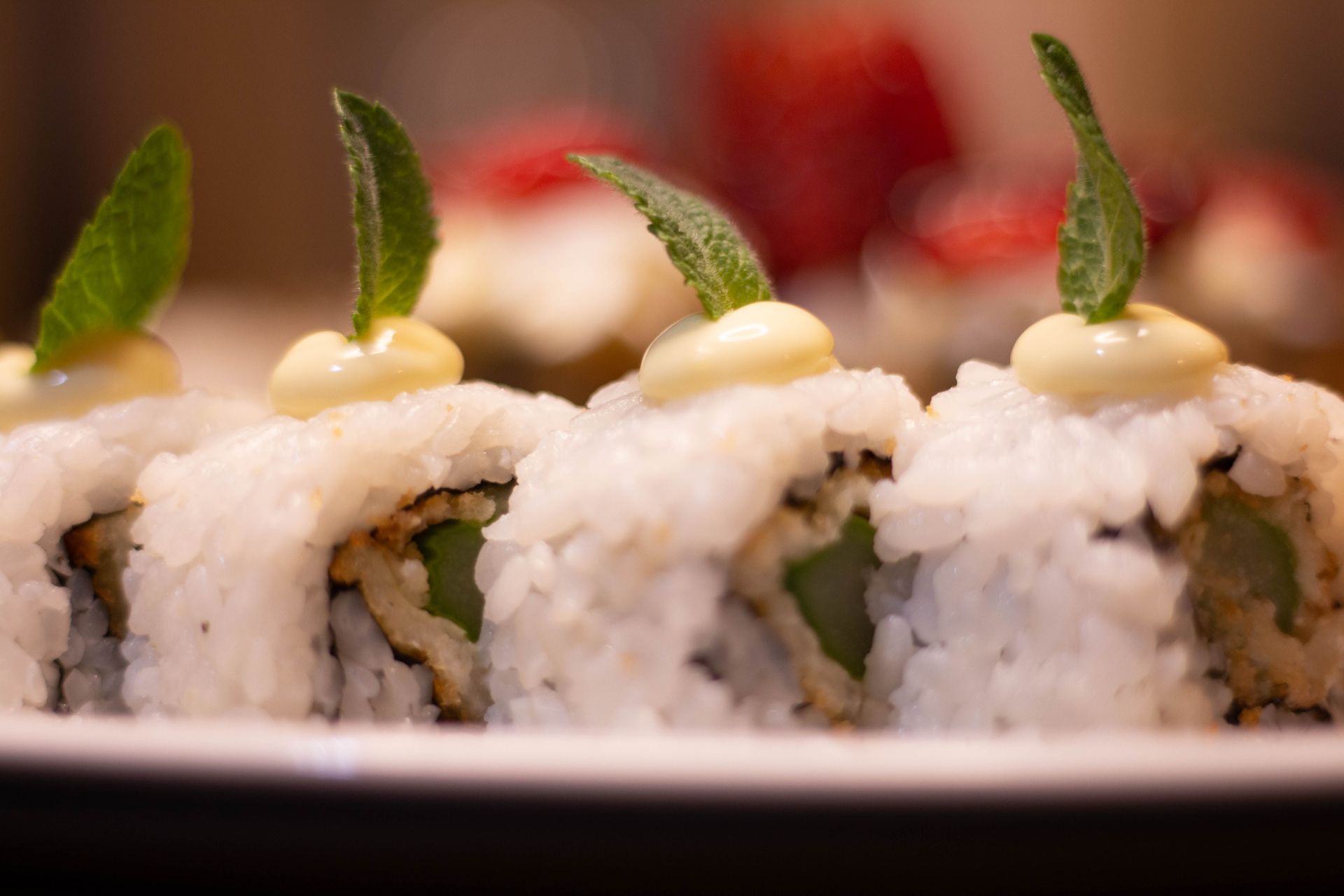 Primo piano di involtini di sushi guarniti con erbe aromatiche e salsa cremosa su un piatto.
