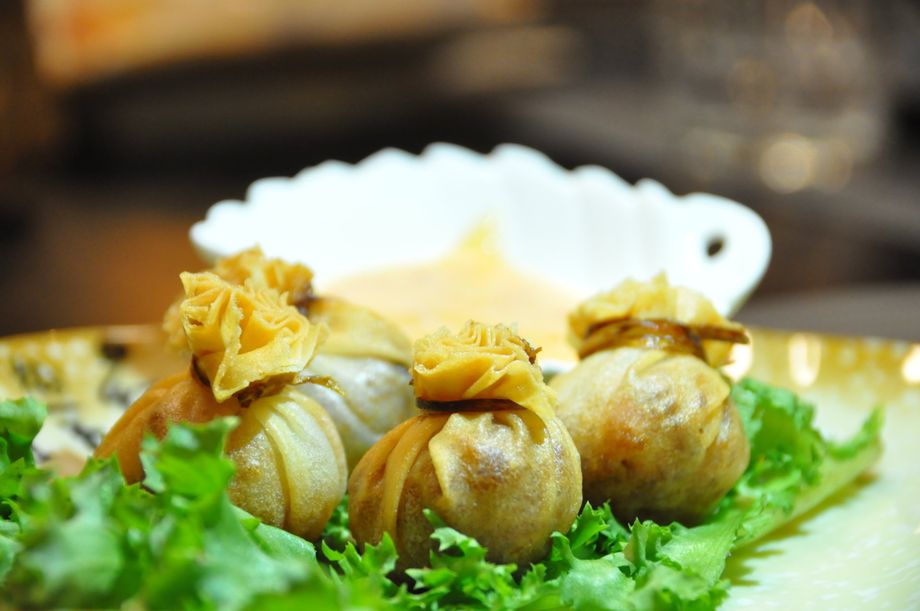 Ravioli ripieni guarniti con erbe aromatiche su un piatto bianco, serviti su foglie di lattuga verde.