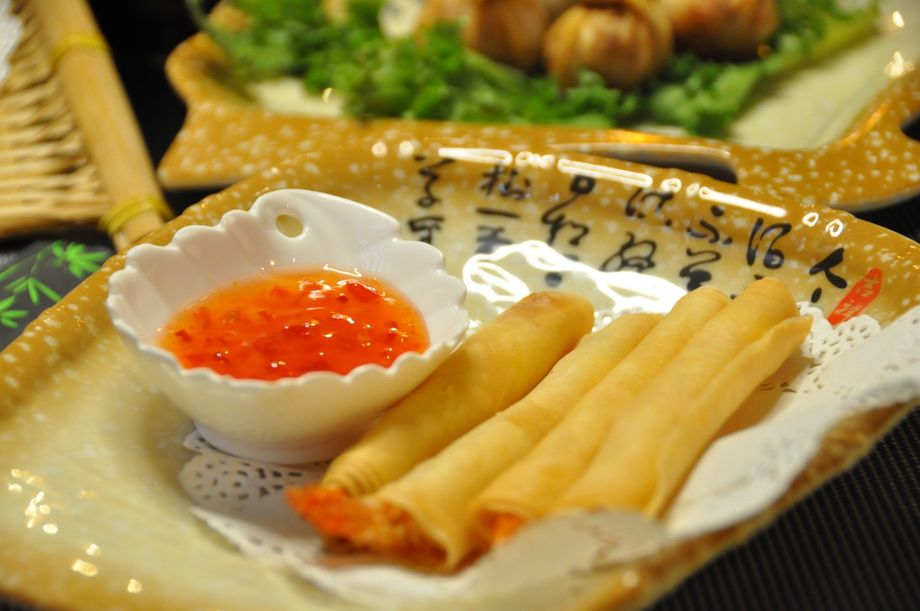 Involtini primavera fritti con una ciotolina di salsa all'arancia su un piatto decorativo.