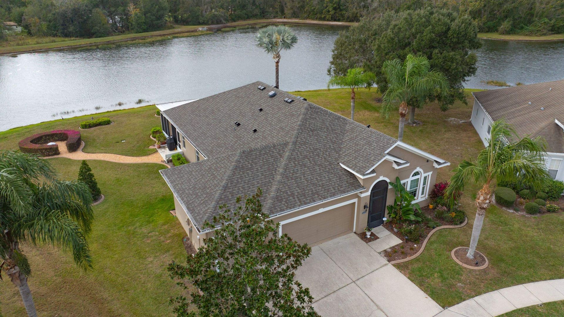 Front aerial view of a home in Palm Cove, Wesley Chapel with a new CertainTeed Landmark Weathered Wood architectural shingle roof overlooking a lake.