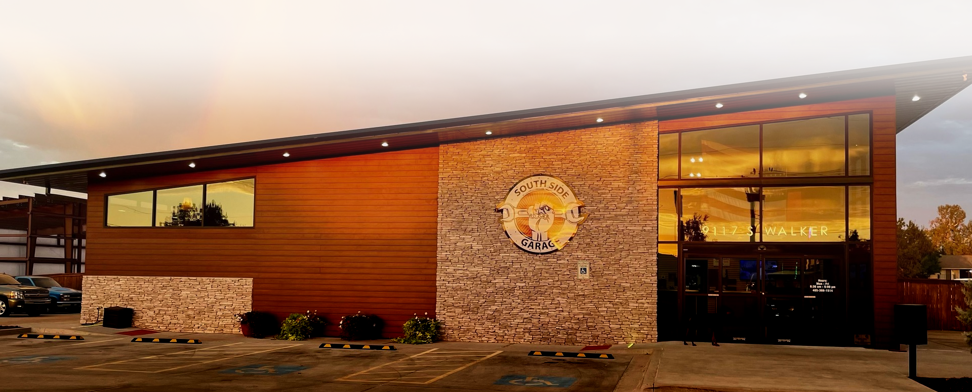 Exterior of a modern building with brown siding and stonework. Large windows reflect an orange sunset | The SouthSide Garage