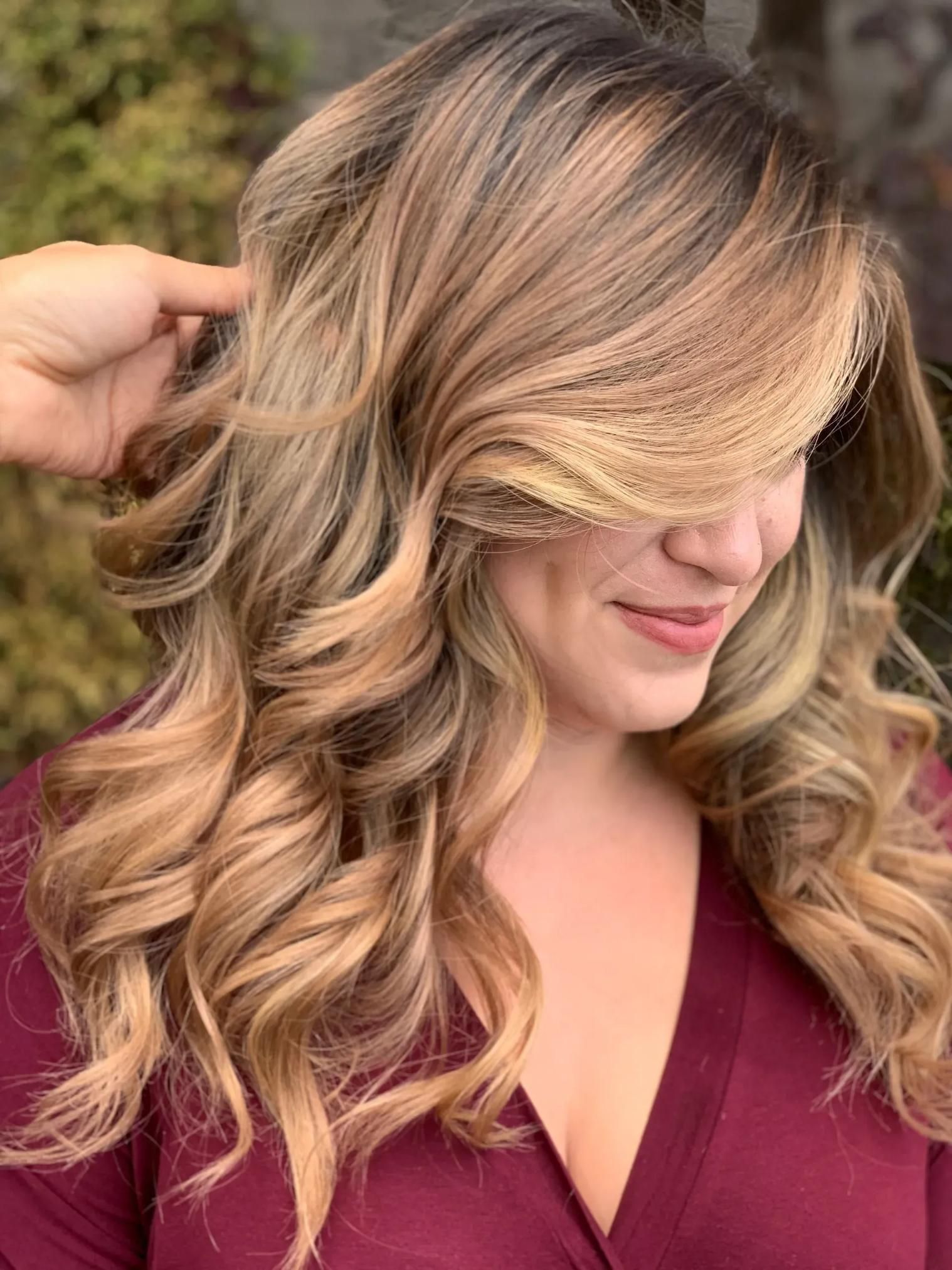Woman with wavy blonde and brown hair, smiling slightly. Someone's hand is in her hair.