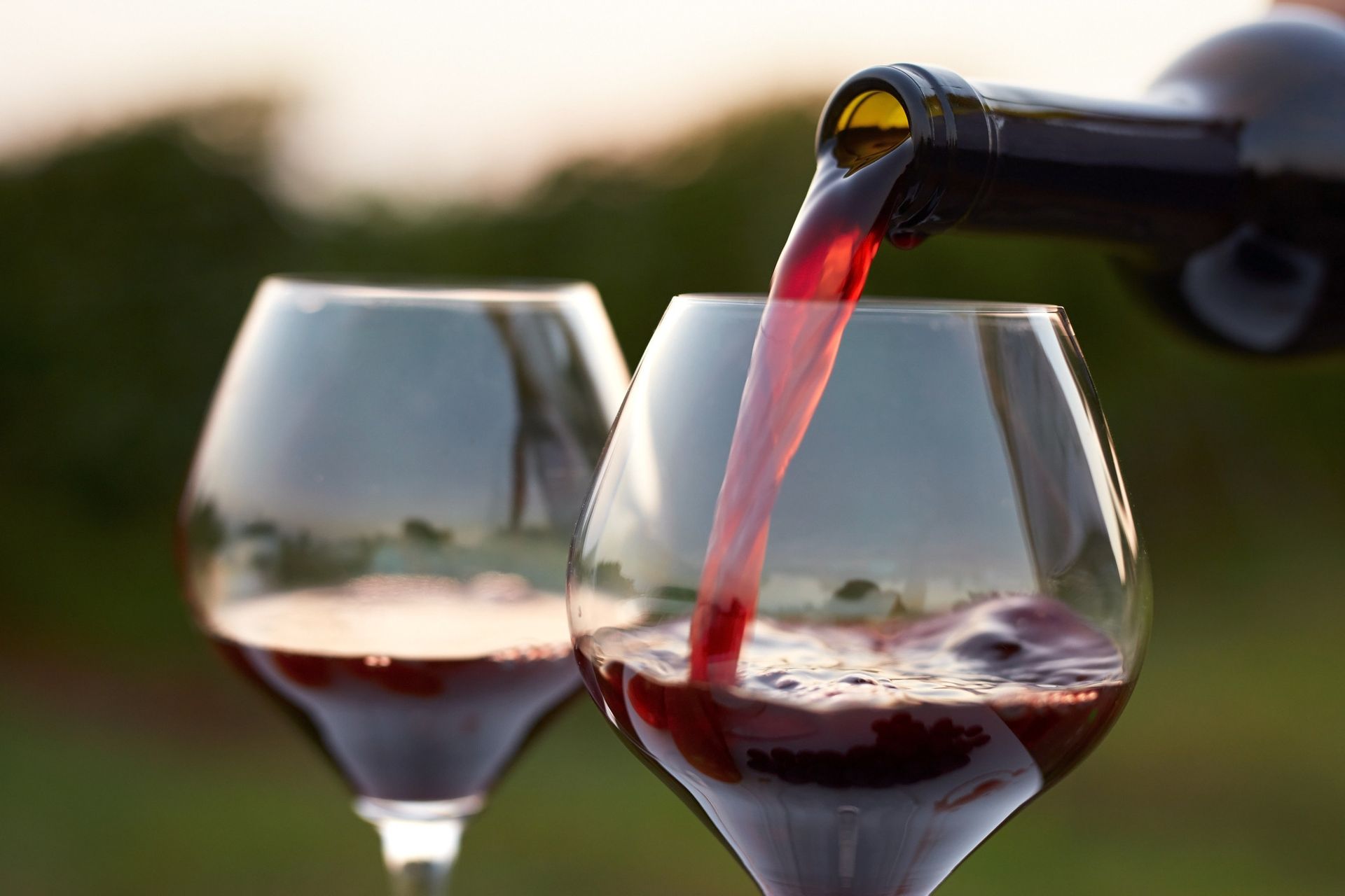 Red wine being poured from a bottle into a glass, with a second glass in the foreground.