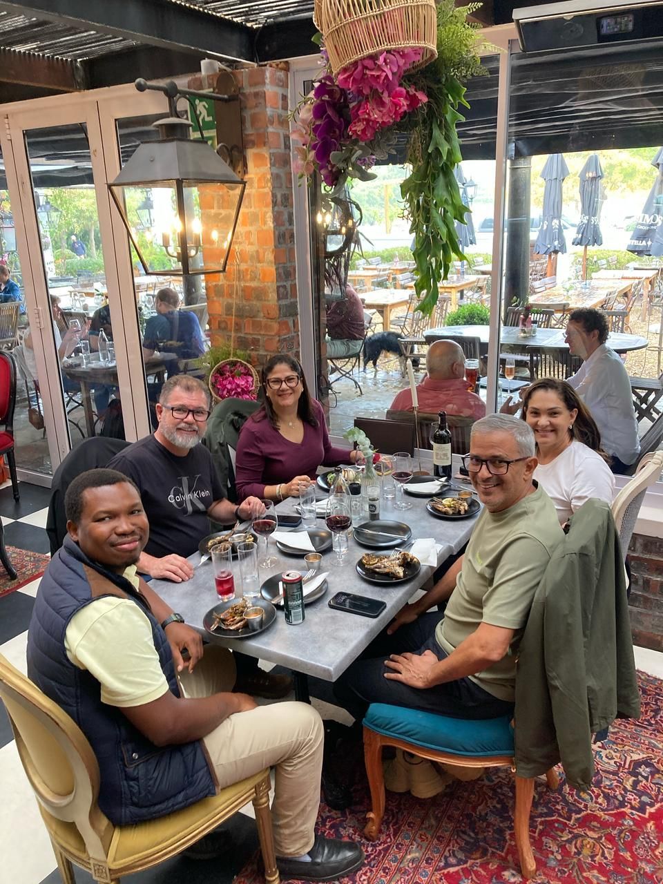 Grupo de seis pessoas sentadas ao redor de uma mesa em um restaurante. Elas sorriem e olham para a câmera.