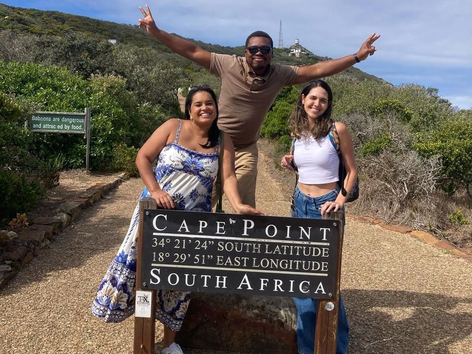 Três pessoas posando na placa de Cape Point, na África do Sul, sorrindo.