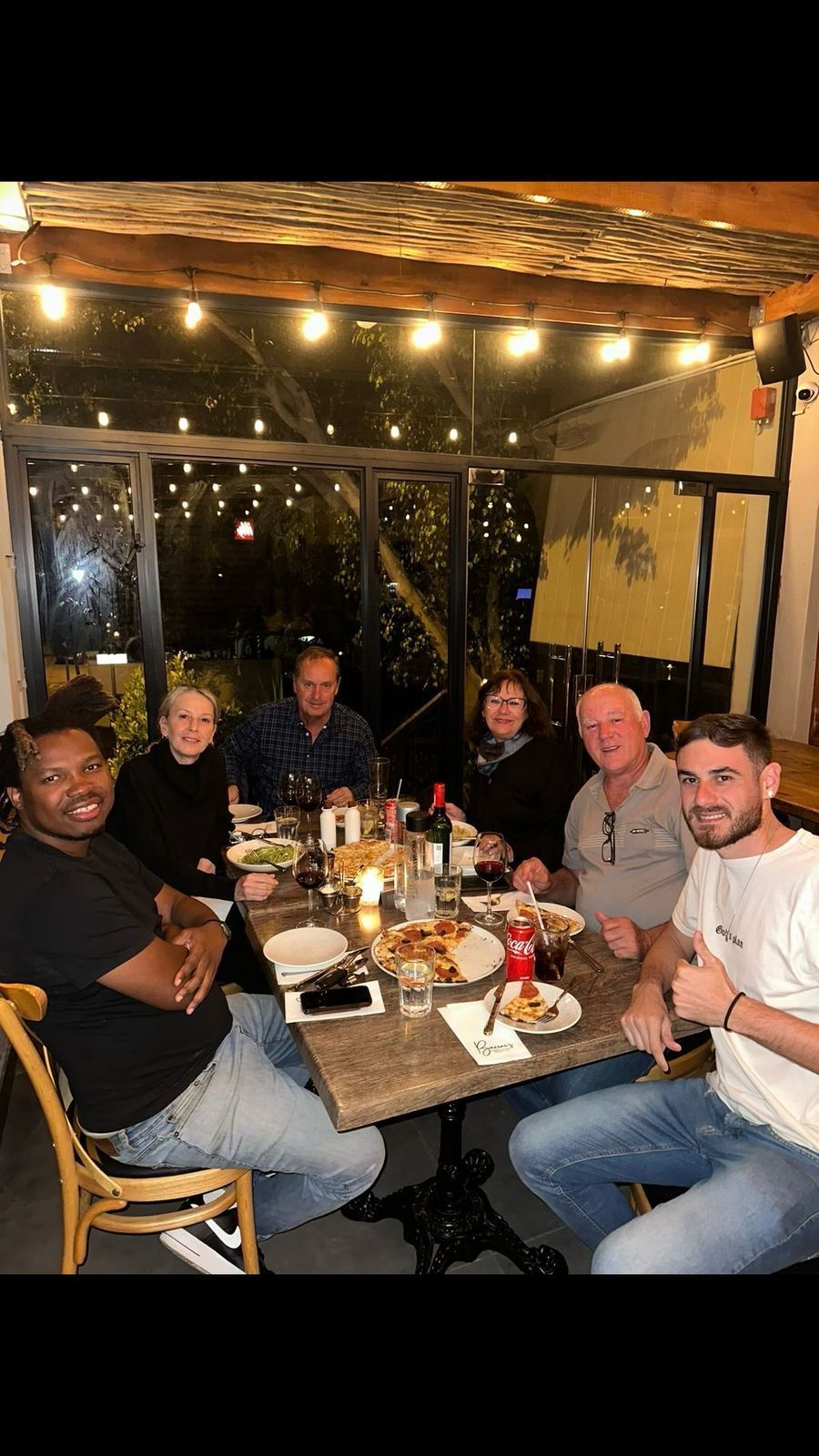 Um grupo de seis pessoas em um restaurante, sorrindo ao redor de uma mesa com comida.