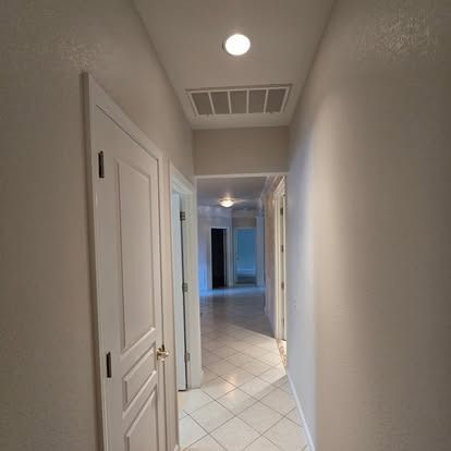 Hallway with white walls, doors, and tile floor, leading to a room at the end.