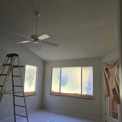 Interior room with a ceiling fan, ladder, and covered windows.