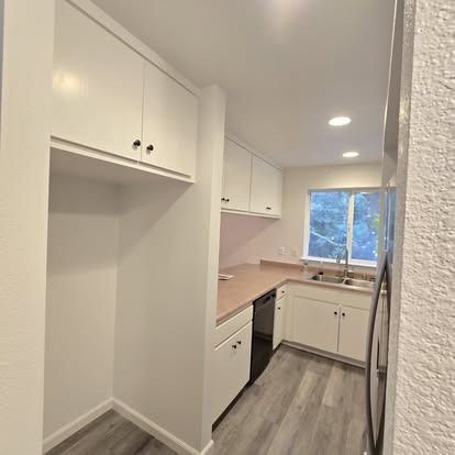 Kitchen with white cabinets, light countertops, and wood-look flooring. Window view of trees.