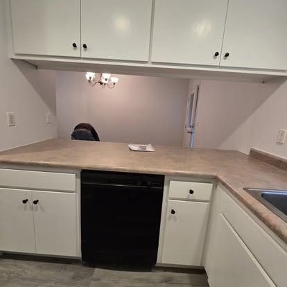 Kitchen with white cabinets, black dishwasher, and beige countertop.
