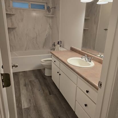 Bathroom with white vanity, sink, tub, and toilet; gray wood-look floor.