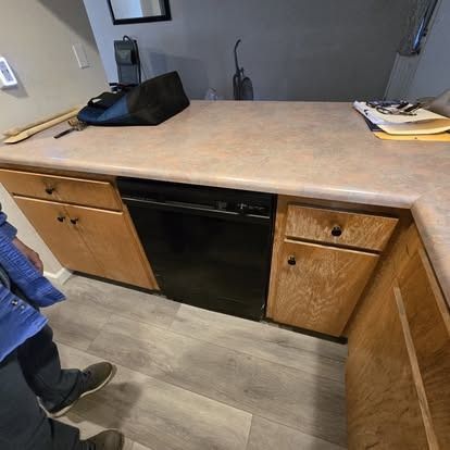 Kitchen with light wood cabinets, black dishwasher, beige countertop, and gray flooring.
