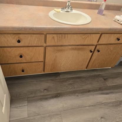 Bathroom vanity with sink, light wood cabinets, and gray flooring.