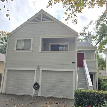Two-story light gray house with two garage doors and a red front door up stairs.