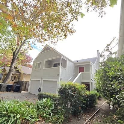 Two-story house with light grey siding, red door, garage, and trees in the front yard.