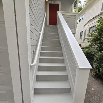 Staircase leading up to a red door of a building, with white handrails and gray steps.