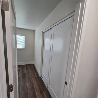 A narrow hallway with a closet and a door. Wood floor and a window visible in the distance.
