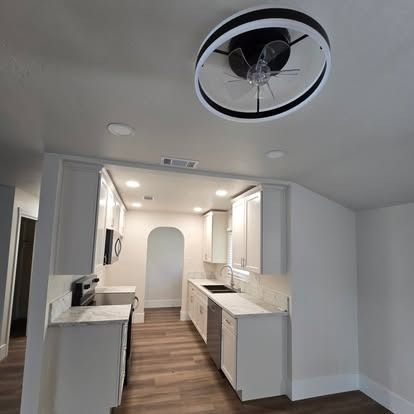 Modern kitchen with white cabinets, stainless steel appliances, and a circular ceiling fan.