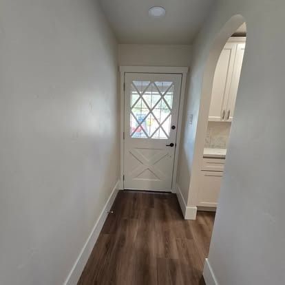 Narrow hallway with a white door at the end and an arched doorway on the right.