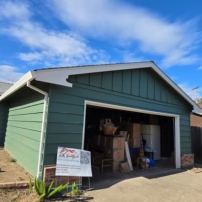Green garage with open door, filled with items, under a blue sky.