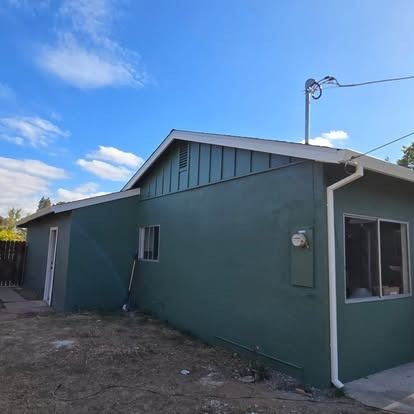 Green-painted house exterior with white trim under a blue sky.