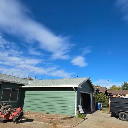Green house with a garage, under a bright blue sky with clouds.