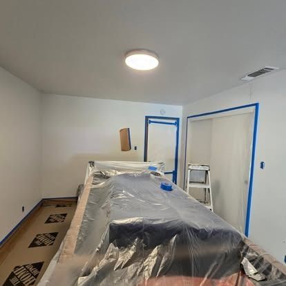 Room being painted: walls are white with blue tape, pool table covered, door and light visible.