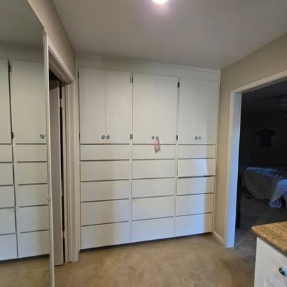 White built-in closet with multiple doors and drawers in a hallway, tan carpet.