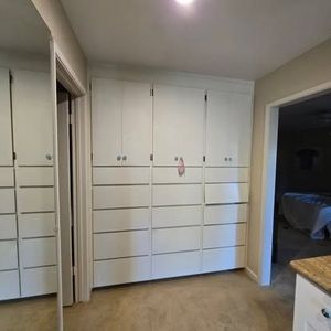 White built-in closet with multiple doors and drawers in a hallway, tan carpet.
