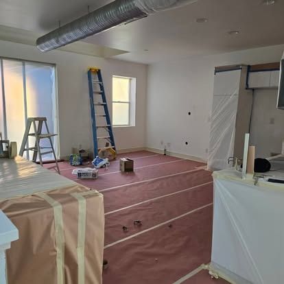 Interior room under construction, with pink flooring, ladder, and white walls covered in plastic.
