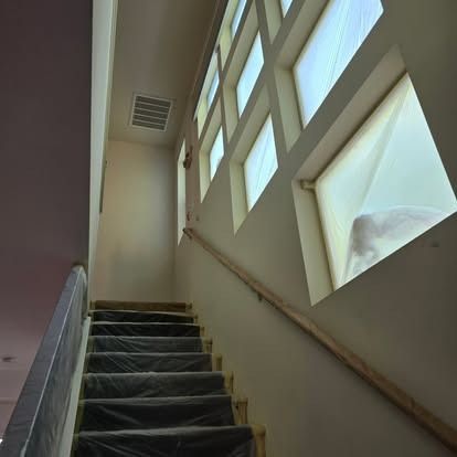 Staircase with plastic-covered steps, railing, and windows with light shining through, in an interior setting.