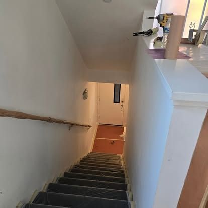 Staircase leading downwards. White walls, wooden handrail, and a door visible at the bottom.
