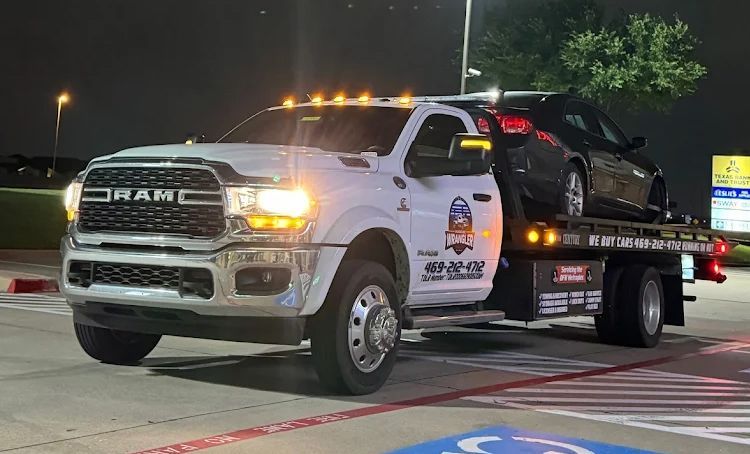 White tow truck with a black car on the bed at night.