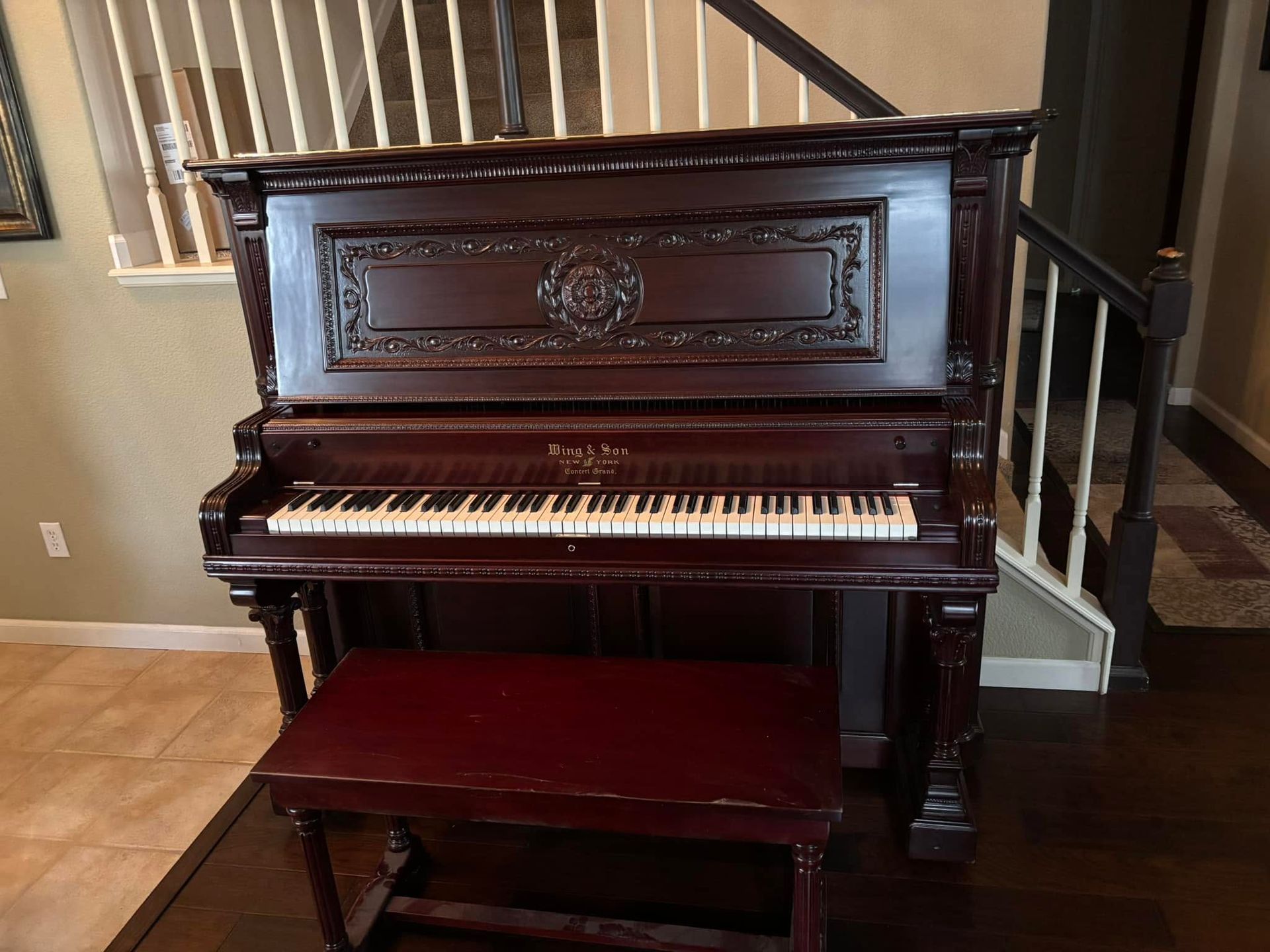 Dark wood upright piano with matching bench in a home interior near a staircase.