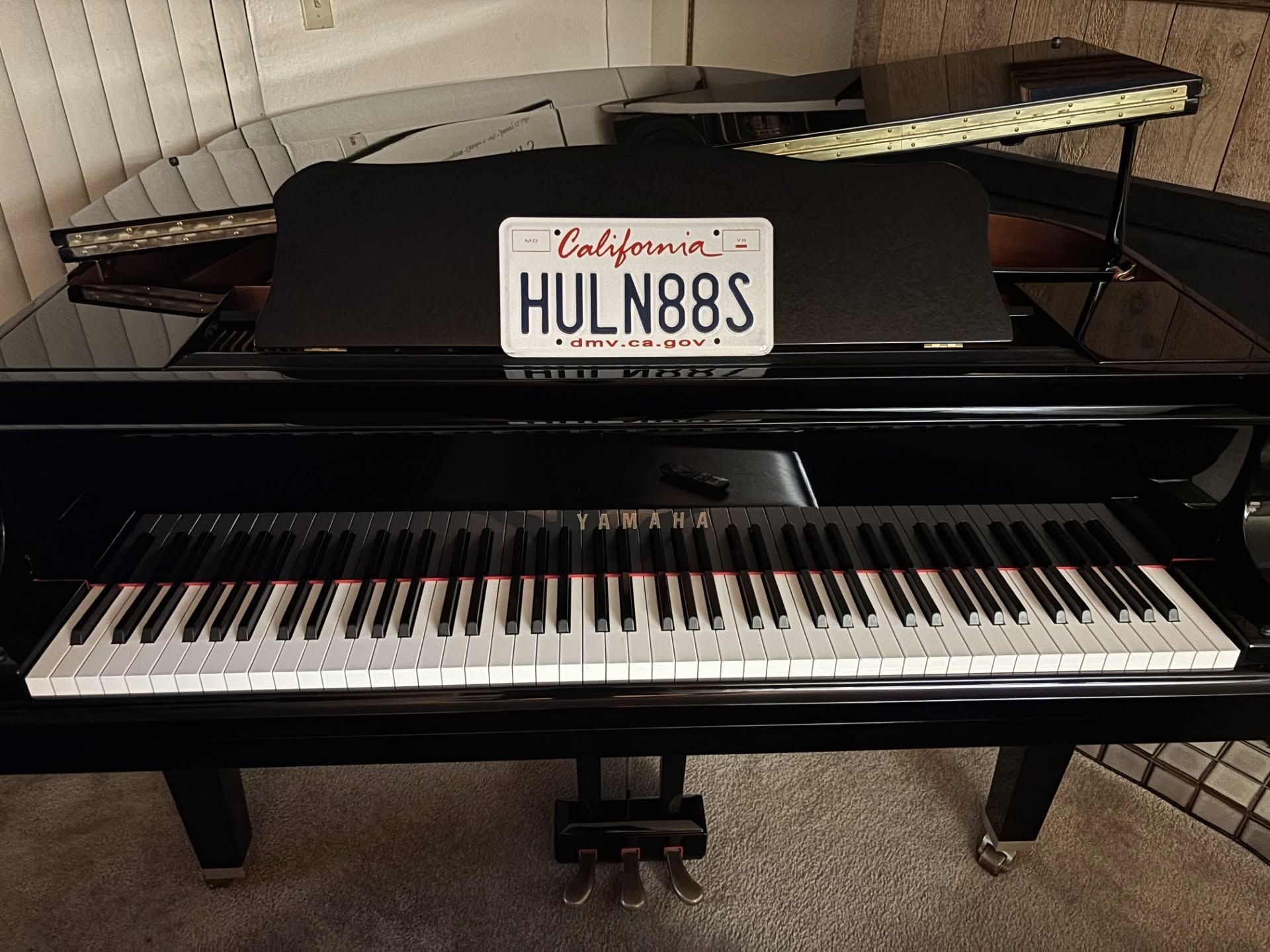 Black grand piano with a California license plate displaying “HULN88” above the keys.
