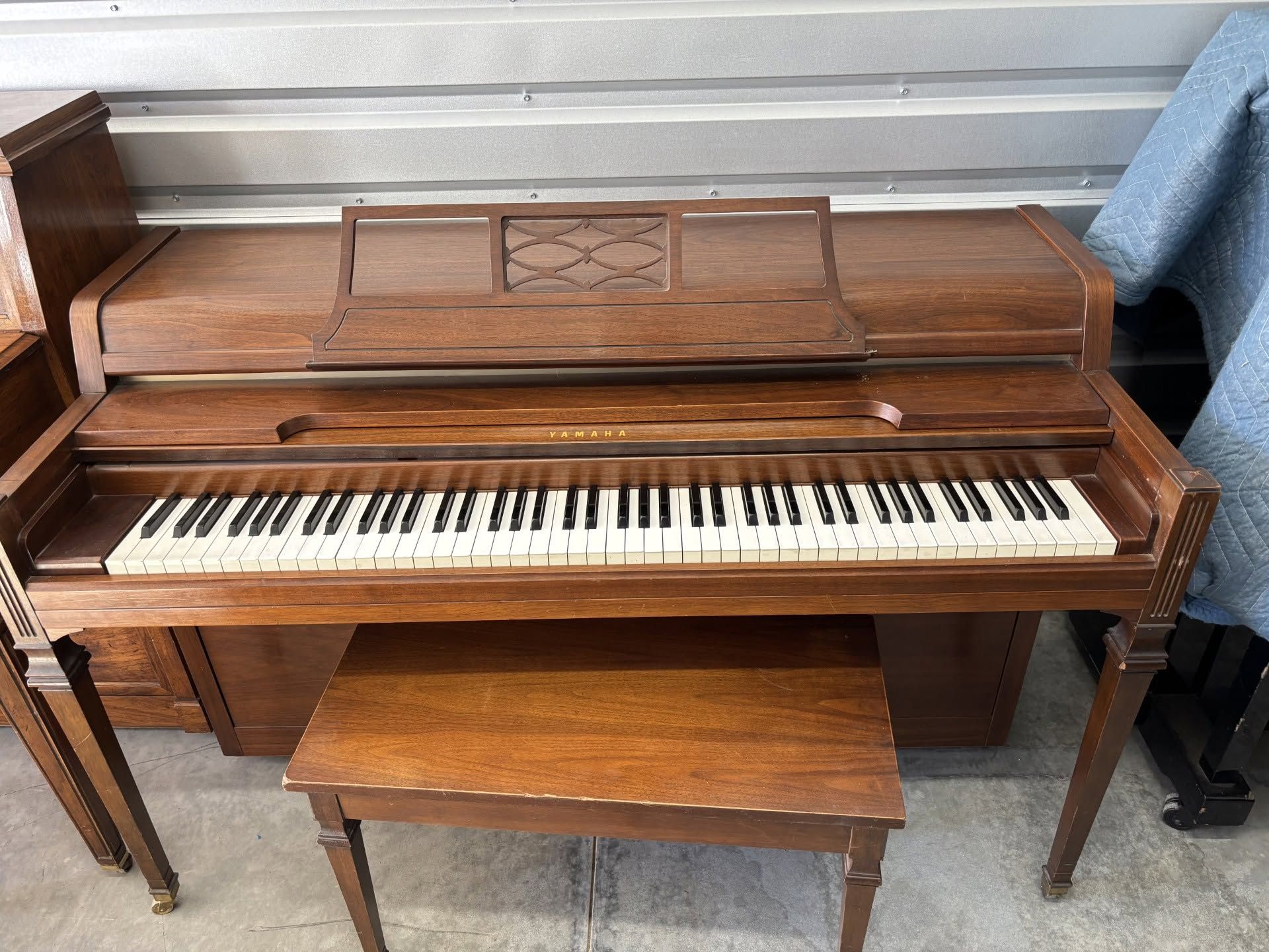 Wooden upright piano with bench, viewed from the front in a garage or storage area
