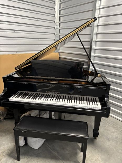 Black grand piano with lid open and bench in a garage or workshop setting
