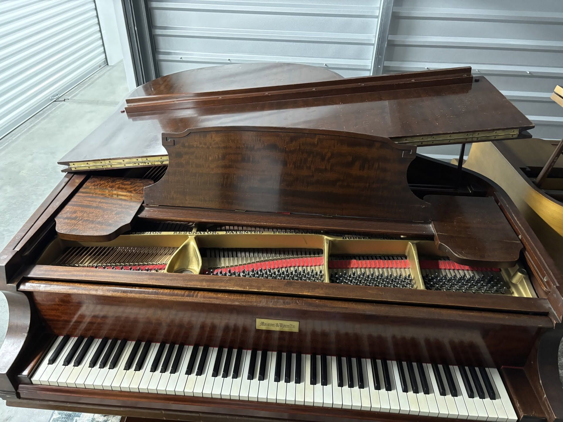 Grand piano with lid open, showing strings and keys in a garage or storage space